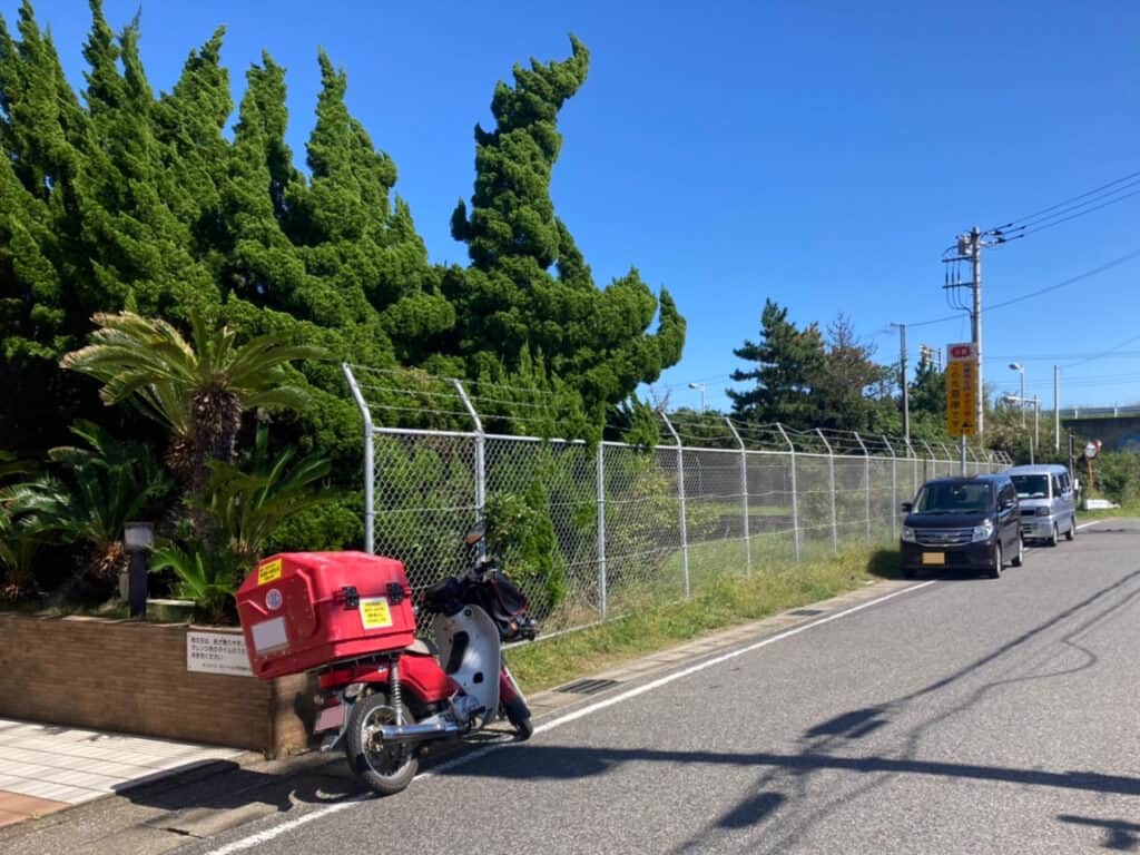 快晴の屋外に停めてある郵便バイクと軽自動車